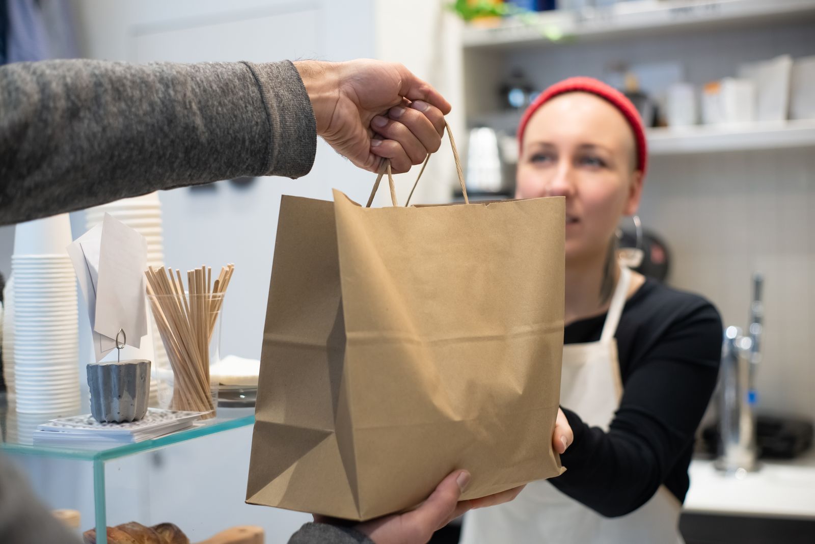 Café worker handing a paper takeaway bag to a customer at the counter