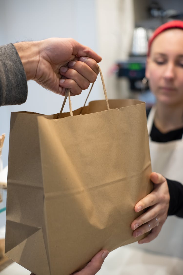 Close-up Of Restaurant Worker Handing A Bag With Takeaway Food To A Client 