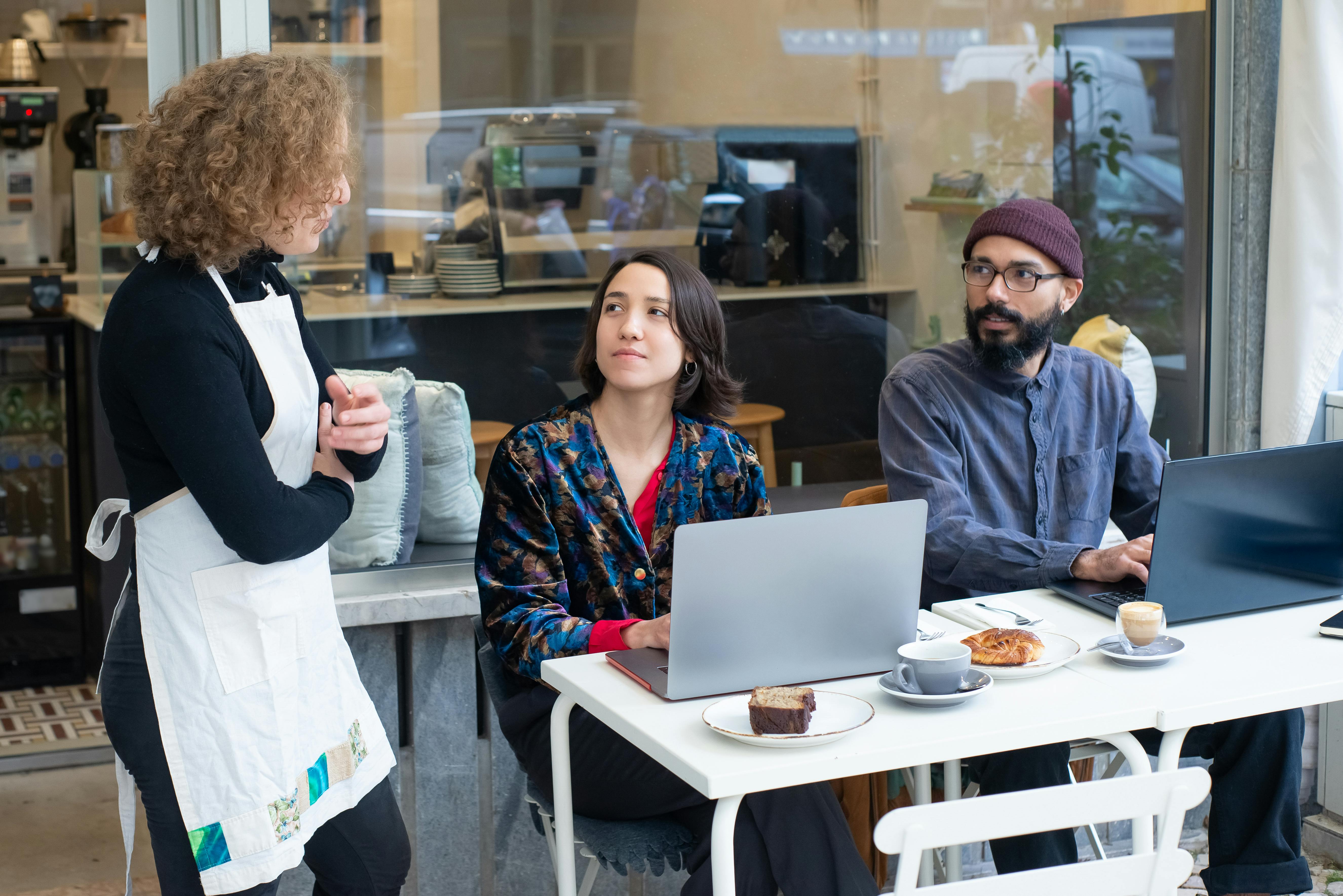 A dynamic outdoor café setting in Portugal with people working on laptops and a waitress serving