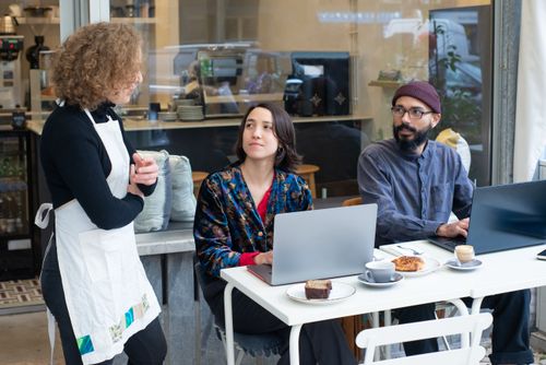 Free A dynamic outdoor café setting in Portugal with people working on laptops and a waitress serving. Stock Photo