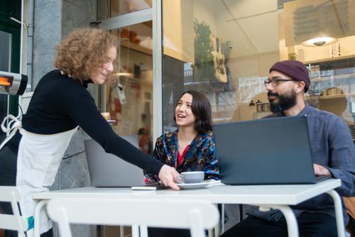 Free Two adults working remotely at a Portugal café, served by a waitress. Stock Photo