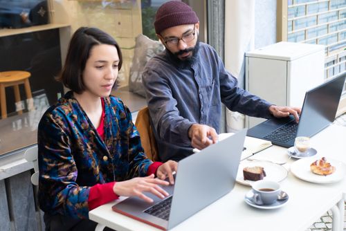Free Two adults working on laptops in a cozy café, enjoying coffee and pastries. Perfect for remote work themes. Stock Photo
