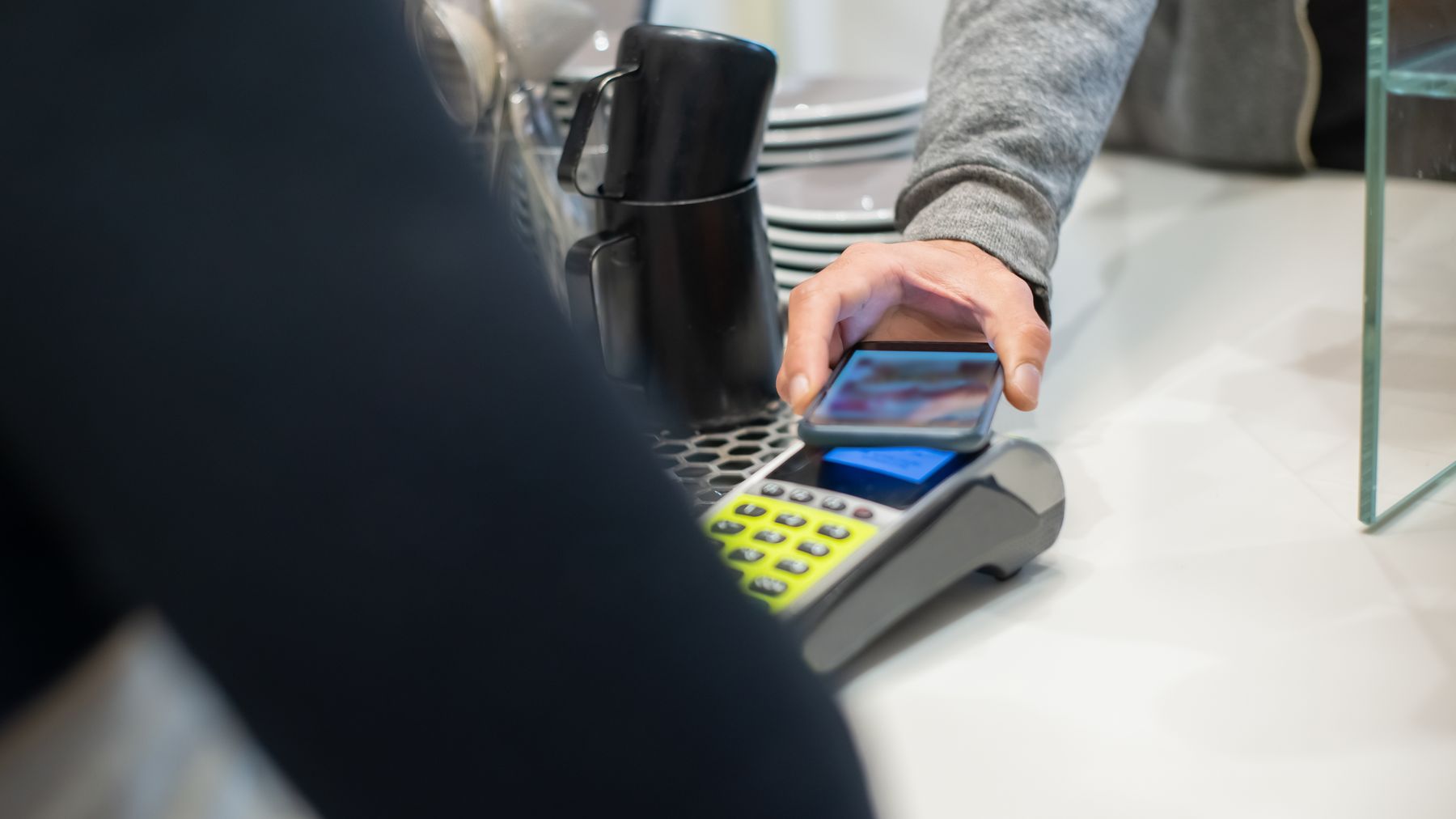 A customer makes a contactless payment using a smartphone at a café, showcasing modern digital transactions.
