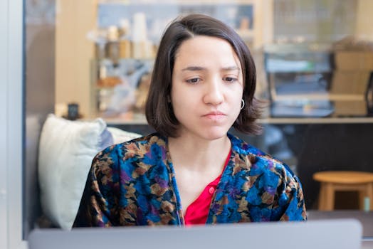 A woman intently working on her laptop in a cafe, captured indoors.