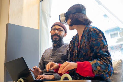 Free Man Sitting Beside a Woman Wearing Virtual Reality Headset Stock Photo