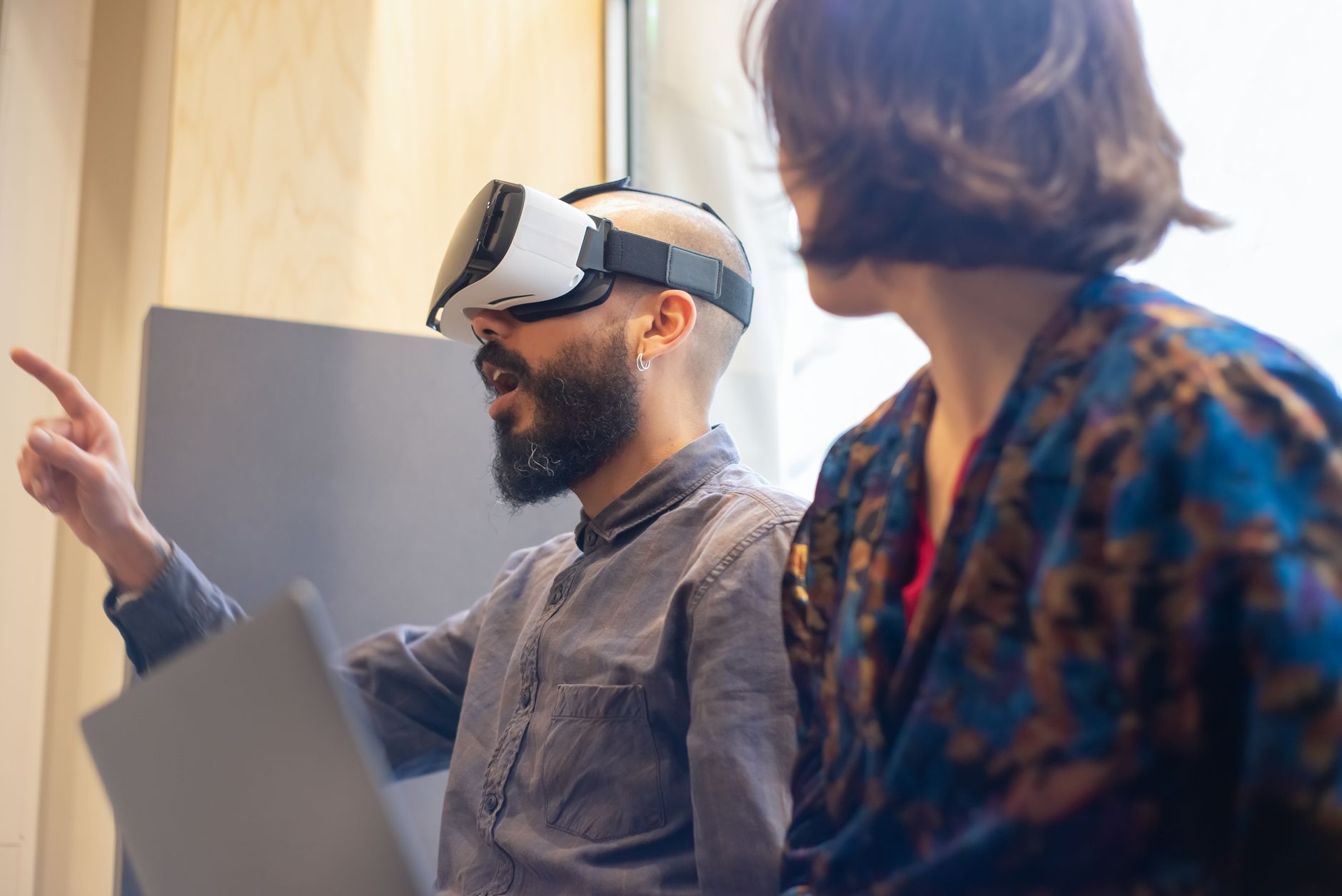 A man with a beard and a woman exploring virtual reality using a headset indoors.