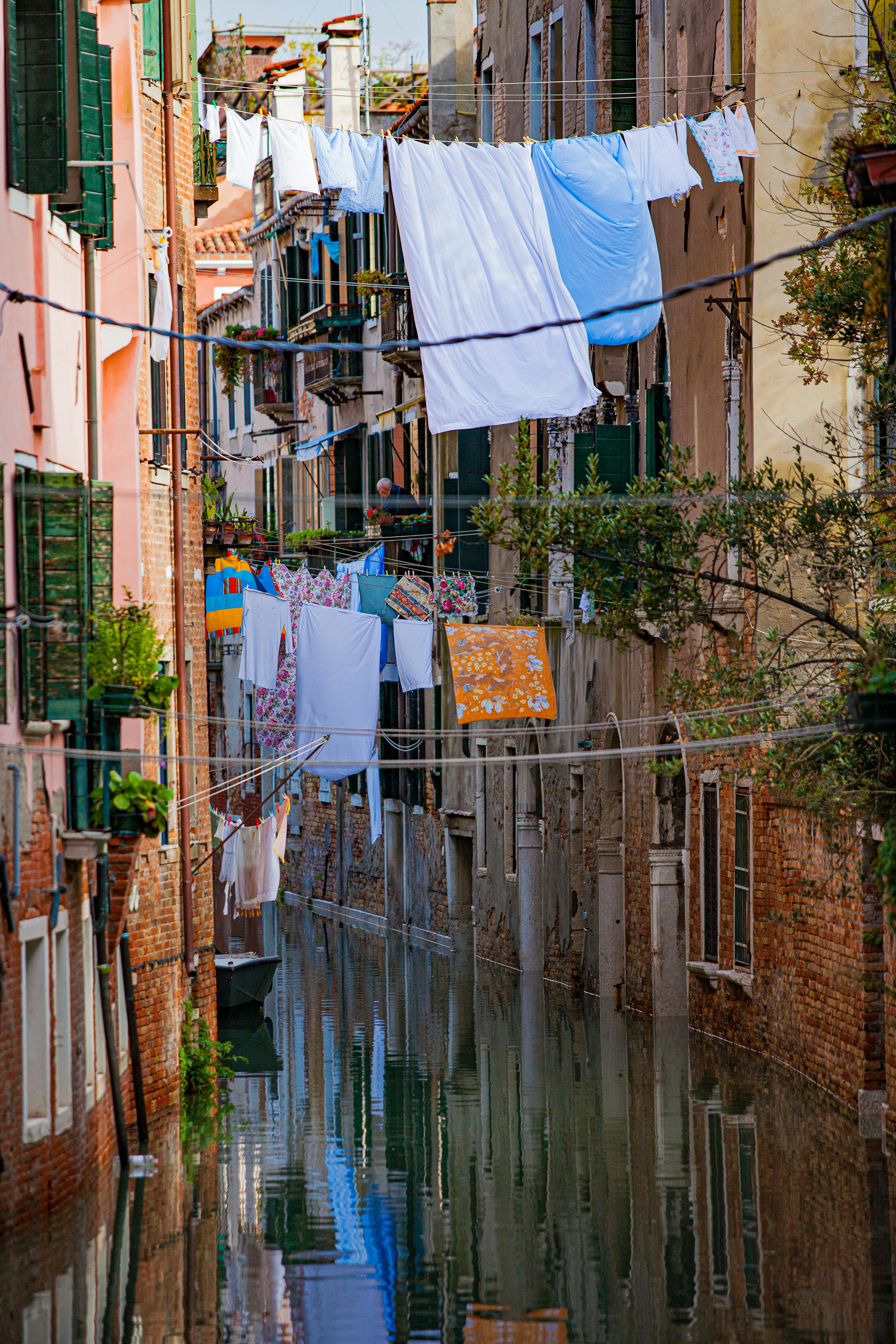 Charming scene of vibrant laundry hanging over a narrow canal in Venice, Italy with reflections.