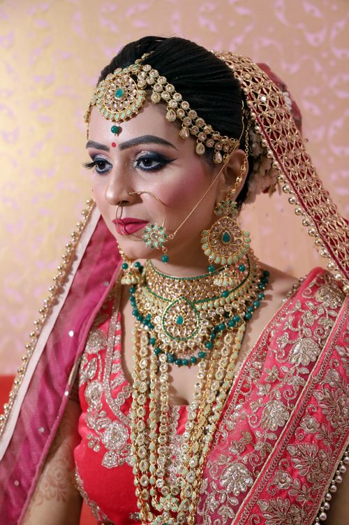 Free Portrait of charming emotionless Indian bride in traditional costume with makeup and traditional golden accessories and beads on gentle pink background Stock Photo