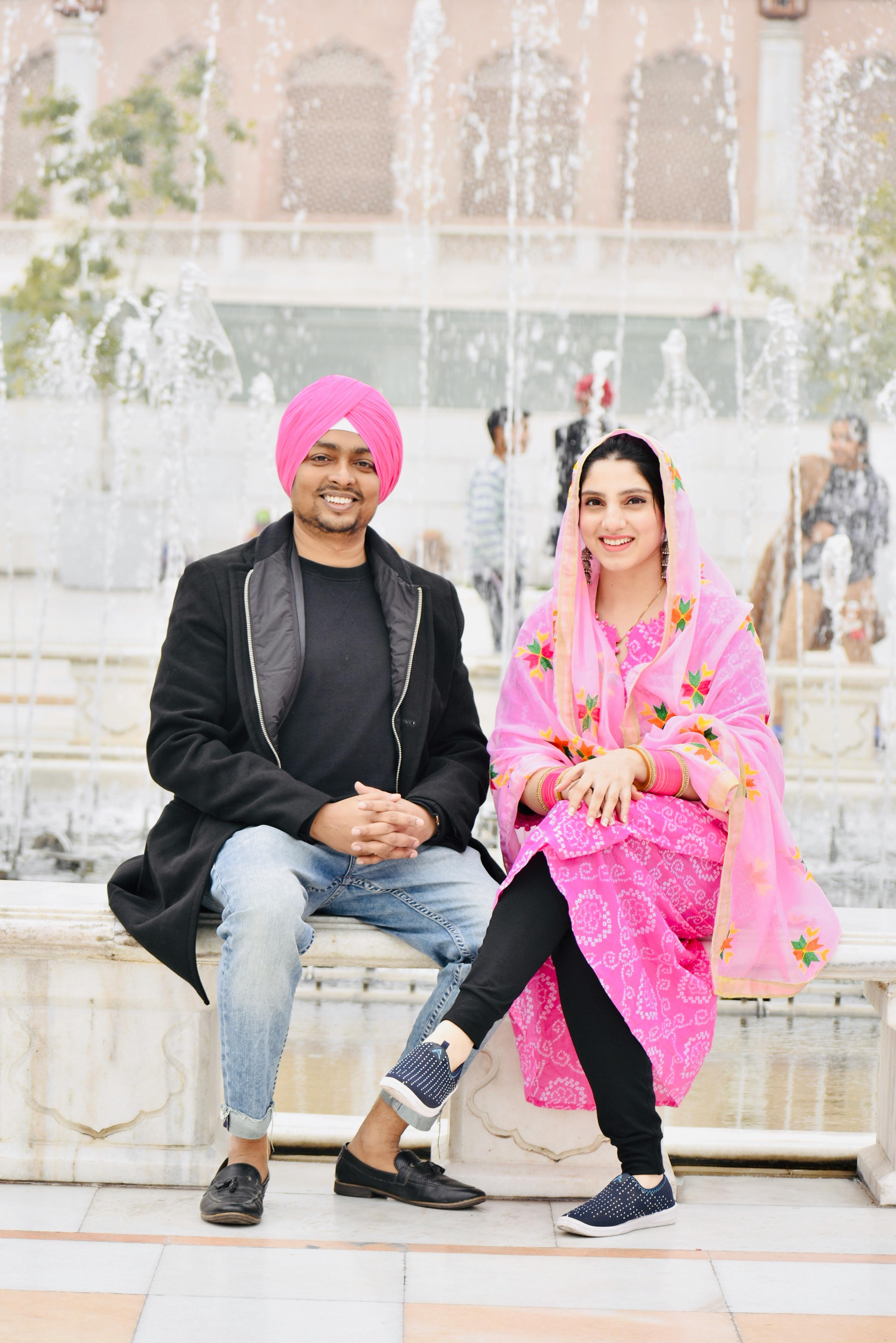 Cheerful Indian couple in traditional attire sitting by a fountain outdoors.
