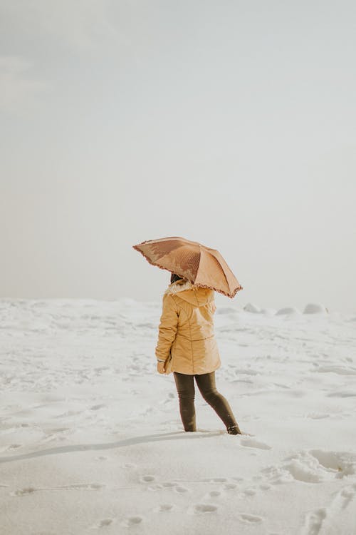 Woman with umbrella standing on snow in sunny weather