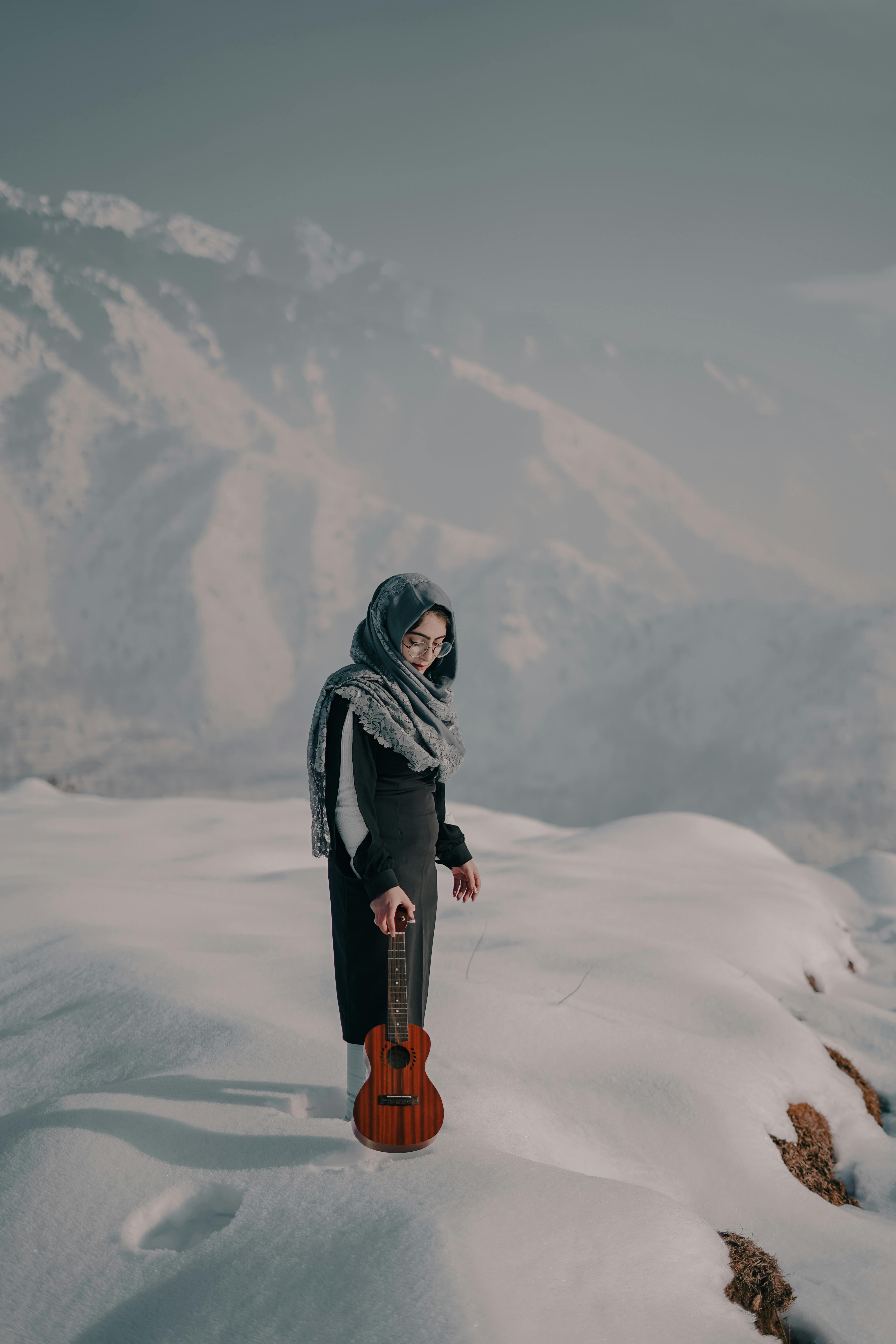 female musician with guitar standing on snowy mountain