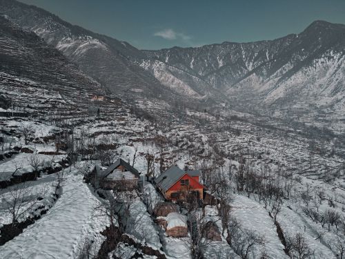 Free Small residential buildings among bare trees located in mountainous valley surrounded by rocky mountains covered with snow Stock Photo