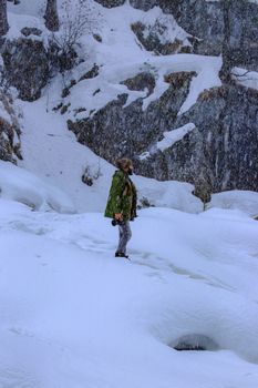 Side view full body of male traveler with photo camera standing on snow against rocky cliff