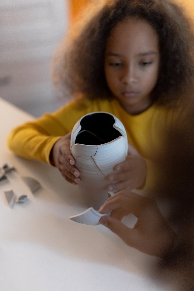 A Young Girl Holding A Broken Vase