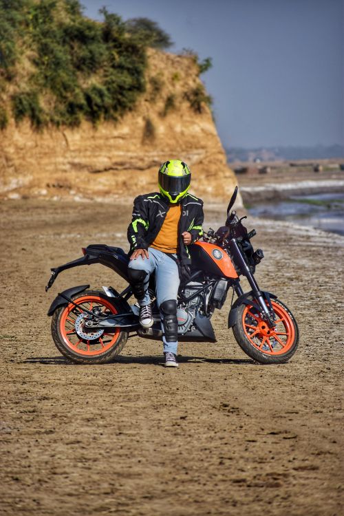 Free Man on motorcycle with vibrant colors posing at a sandy beach in India, showcasing adventure and style. Stock Photo