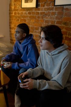 Two teenagers play video games together indoors, focused and relaxed.