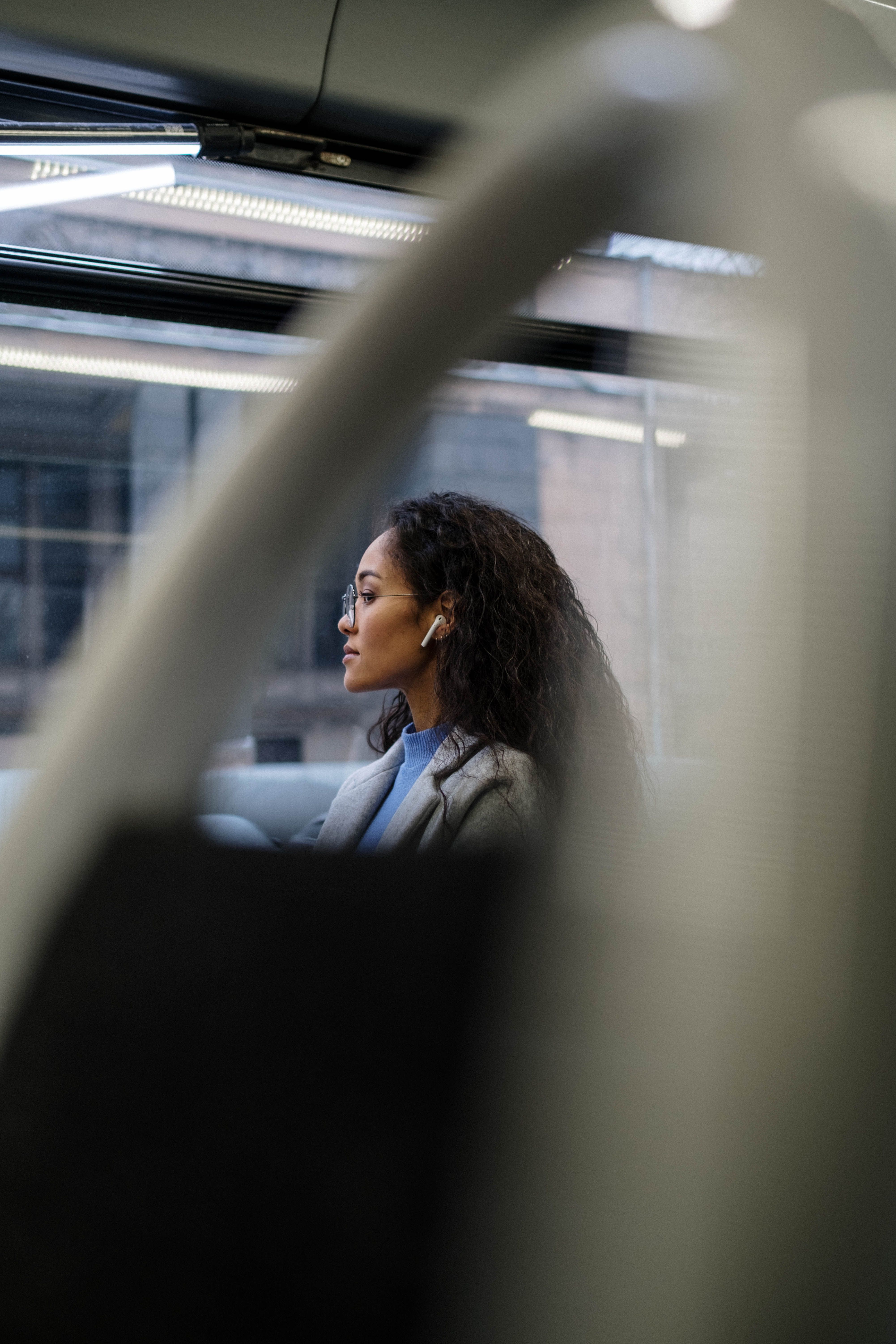 Black woman in a relaxed moment on a city bus gazing out the window with earbuds in