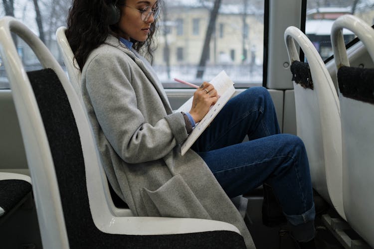 A Woman Sitting Inside A Bus While Writing On A Notebook