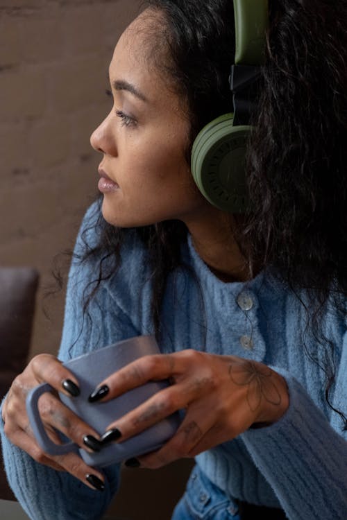 Free Close-up Shot of a Woman Wearing Green Headphones While Holding a Blue Mug Stock Photo