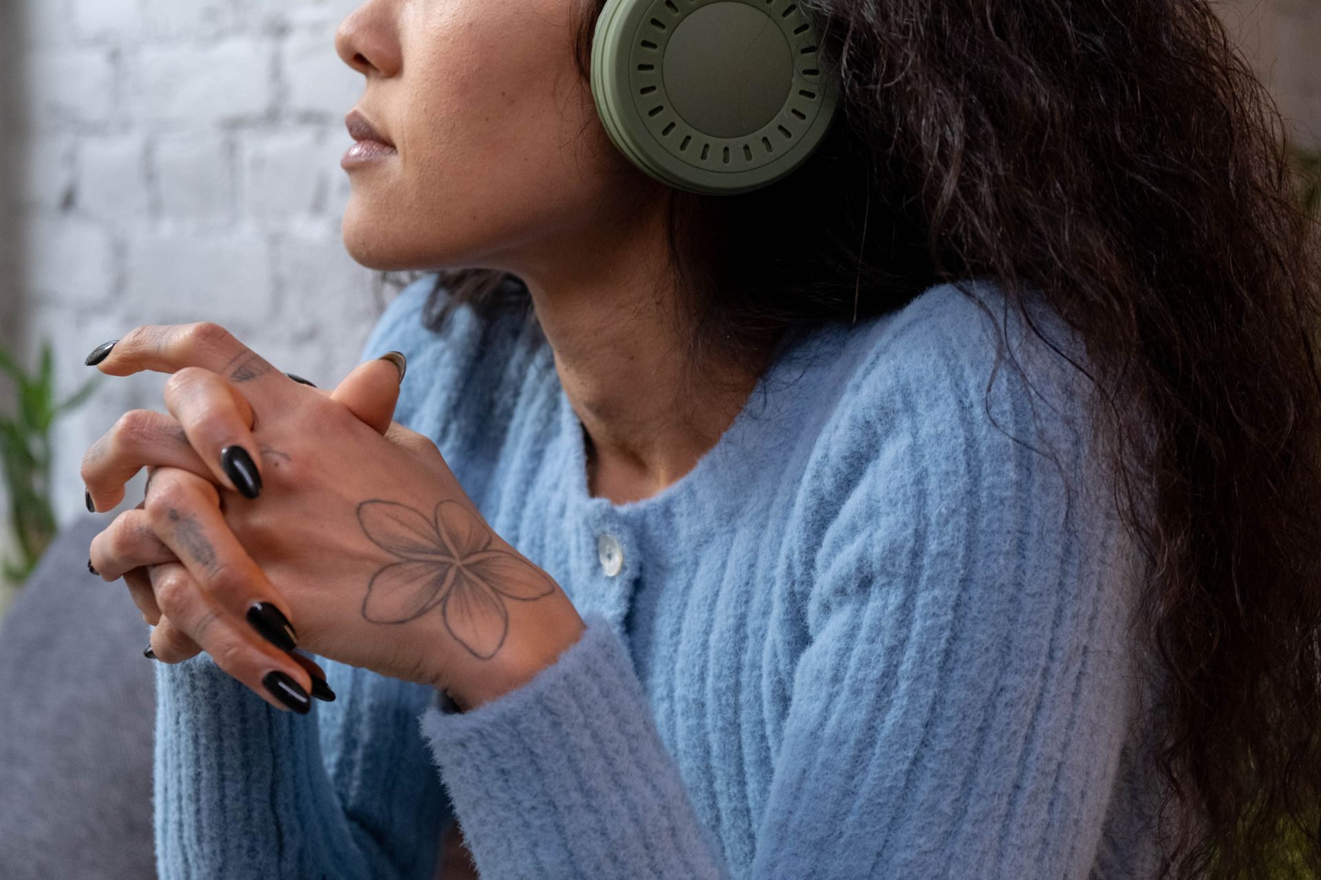 Close-up of a woman listening to music with headphones, wearing a blue sweater and showcasing a floral tattoo on her hand.