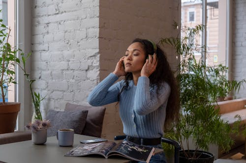 Free A Woman in Blue Sweater Sitting While Holding Her Headphones Stock Photo