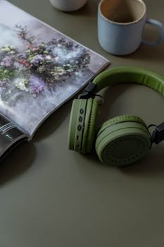 Green headphones and magazine on a table with a mug, creating a casual mood.