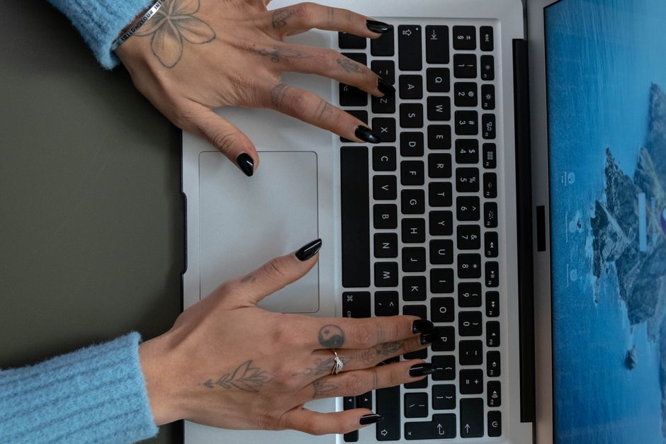 How Oura Ring Sleep Staging Matches Clinical Sleep Studies Close-up of tattooed hands with black nails typing on a laptop keyboard indoors.