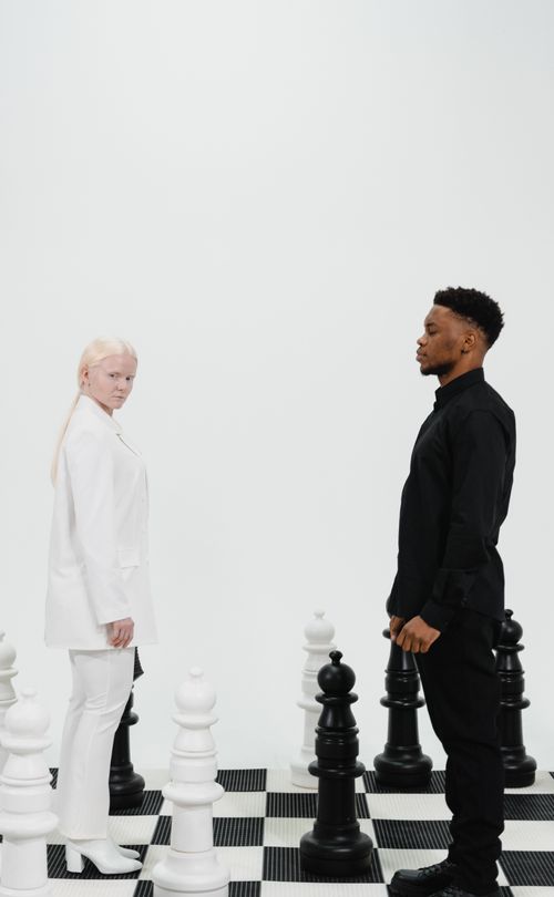 Free Two people stand on a chessboard, representing contrast and strategy. Stock Photo