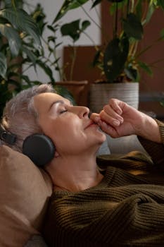 A mature woman with gray hair enjoying music with headphones, relaxing indoors.