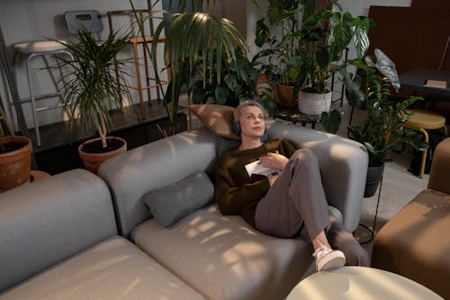 Free Woman Lying on Gray Couch Surrounded with Indoor Plants  Stock Photo