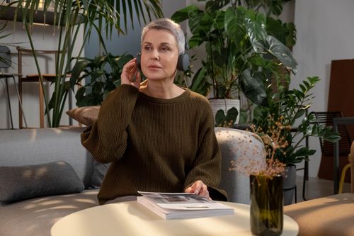 Free A mature woman enjoys music with headphones in a stylish living room filled with lush greenery. Stock Photo