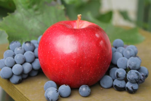 Close-Up Photo of a Red Apple Beside Blueberries