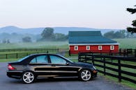 雾气缭绕的早晨，一辆时尚的黑色汽车停在农场里充满活力的红色谷仓旁边