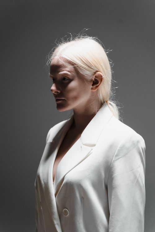 Free Portrait of a woman in a white blazer with platinum hair against a gray background, in a side view pose. Stock Photo