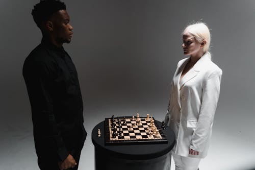 Man in Black Suit and Woman in White Blazer Playing Chess 