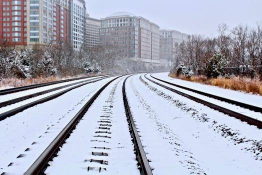 Snow-covered railway tracks amidst modern urban buildings in winter.