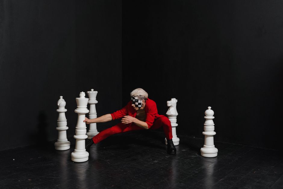 Artistic studio shoot featuring chess pieces and performer in a unique pose.