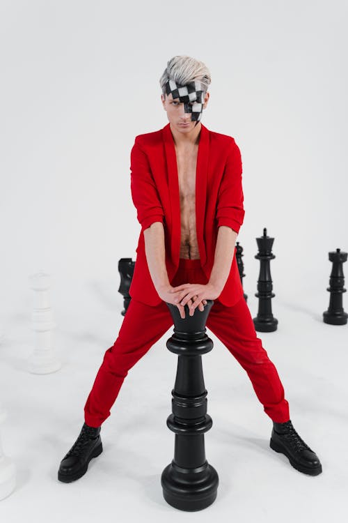 A Man in Red Pants Posing with a Black Chess Piece