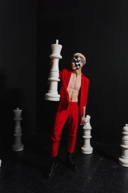 Artistic studio portrait with chess theme, featuring model with face paint and oversized chess pieces.