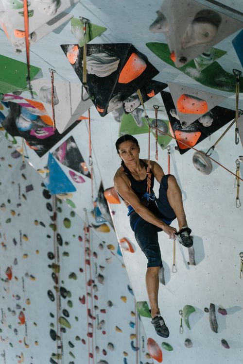 Free Asian woman climbing an indoor rock wall, showcasing extreme sport and agility. Stock Photo