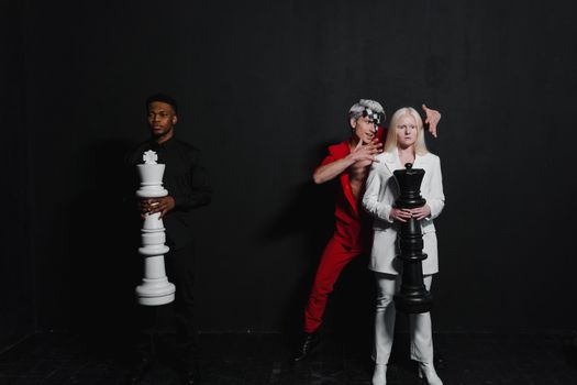 Three people posed indoors with giant chess pieces representing a strategic game concept.