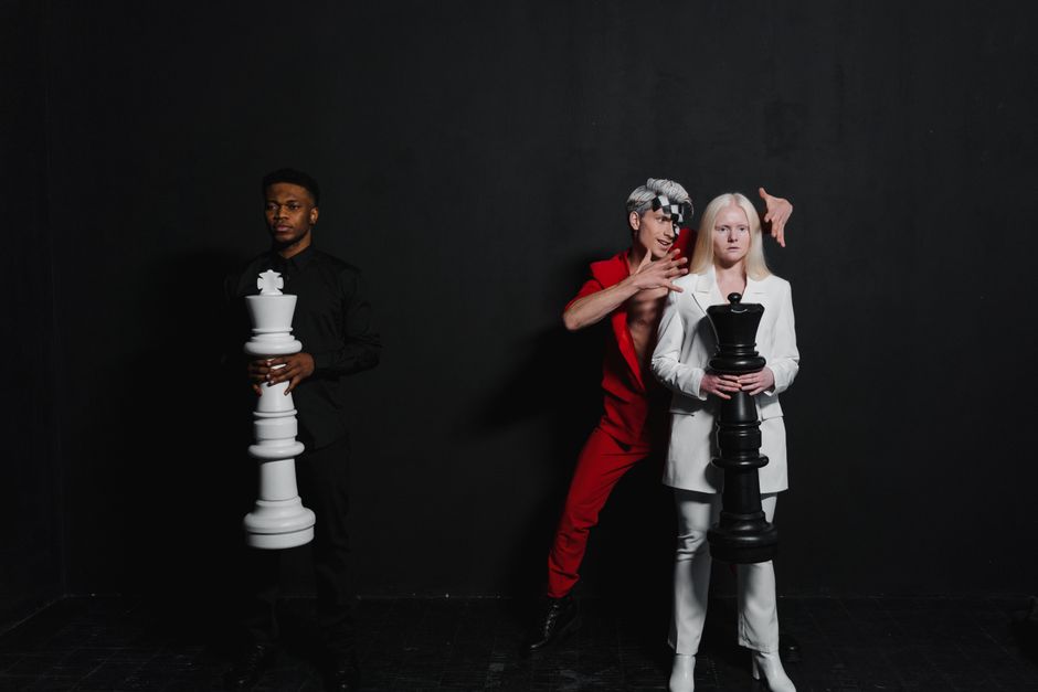 Three people posed indoors with giant chess pieces representing a strategic game concept.