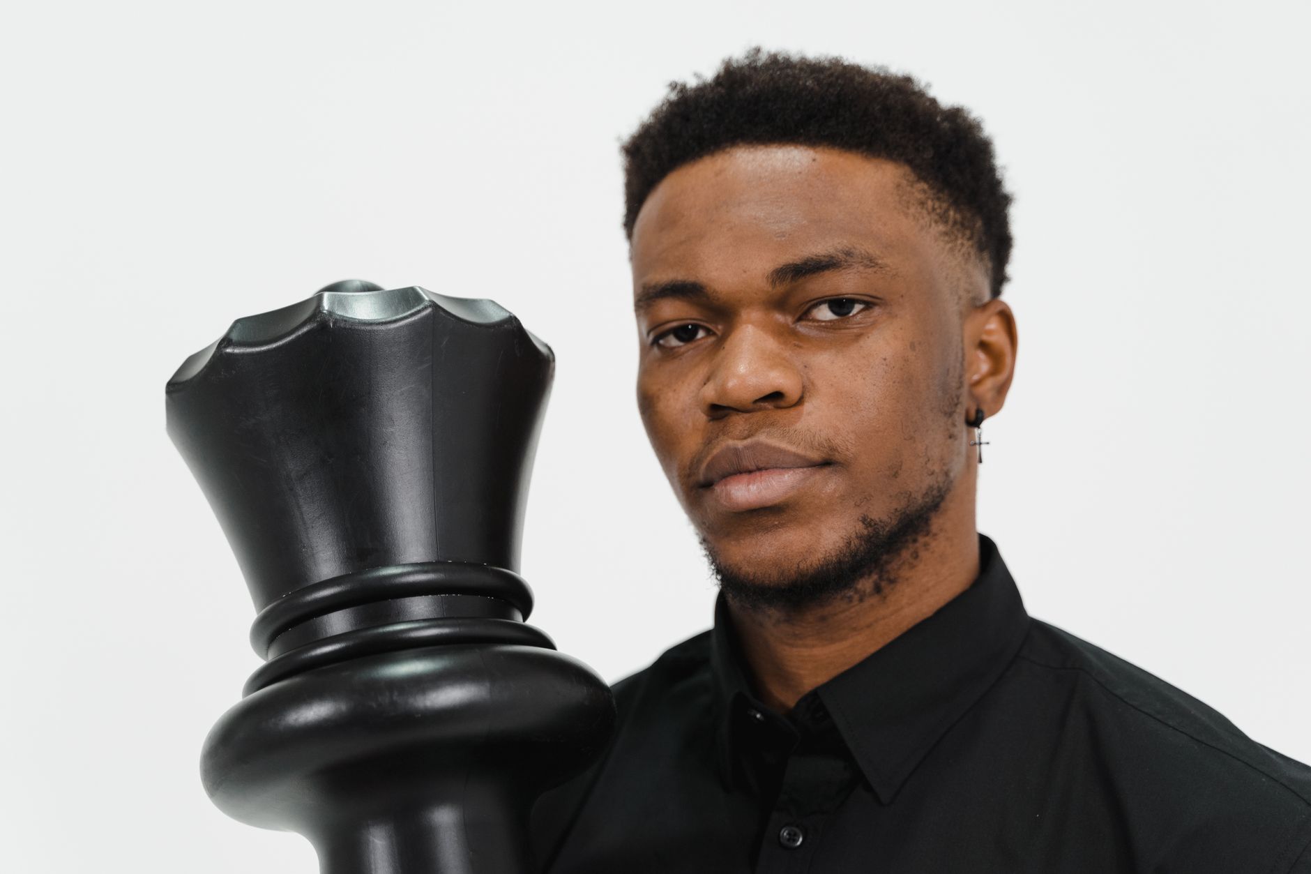 Focused portrait of a man holding a large black chess piece against a white background.