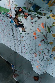 A determined climber scaling an indoor climbing wall with colorful holds, captured from a high angle.