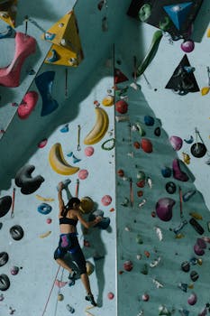 A woman ascends a colorful indoor rock wall in a gym setting, showcasing skill and focus.