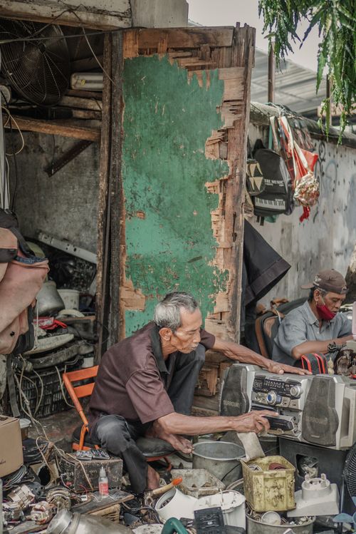 Free An elderly man skillfully repairs a portable stereo in a street workshop setting. Stock Photo