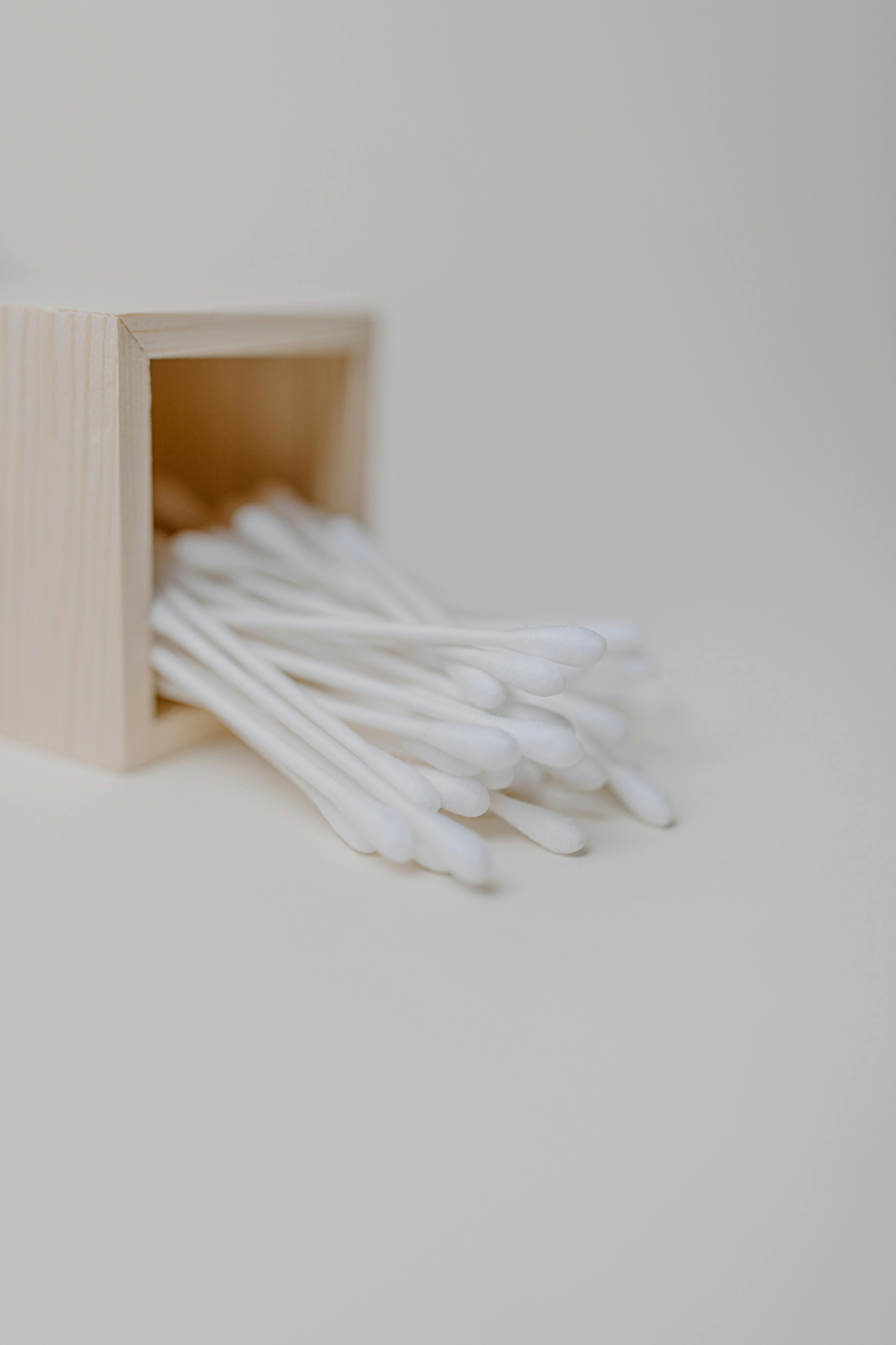 A clean, minimalist image of cotton swabs spilling from a wooden box against a neutral backdrop.