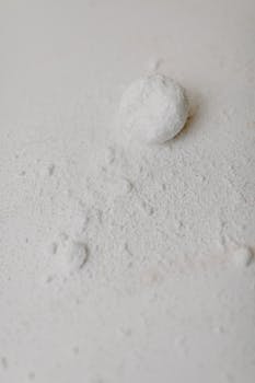 Abstract minimalist image capturing white powder and a ball on a flat surface.