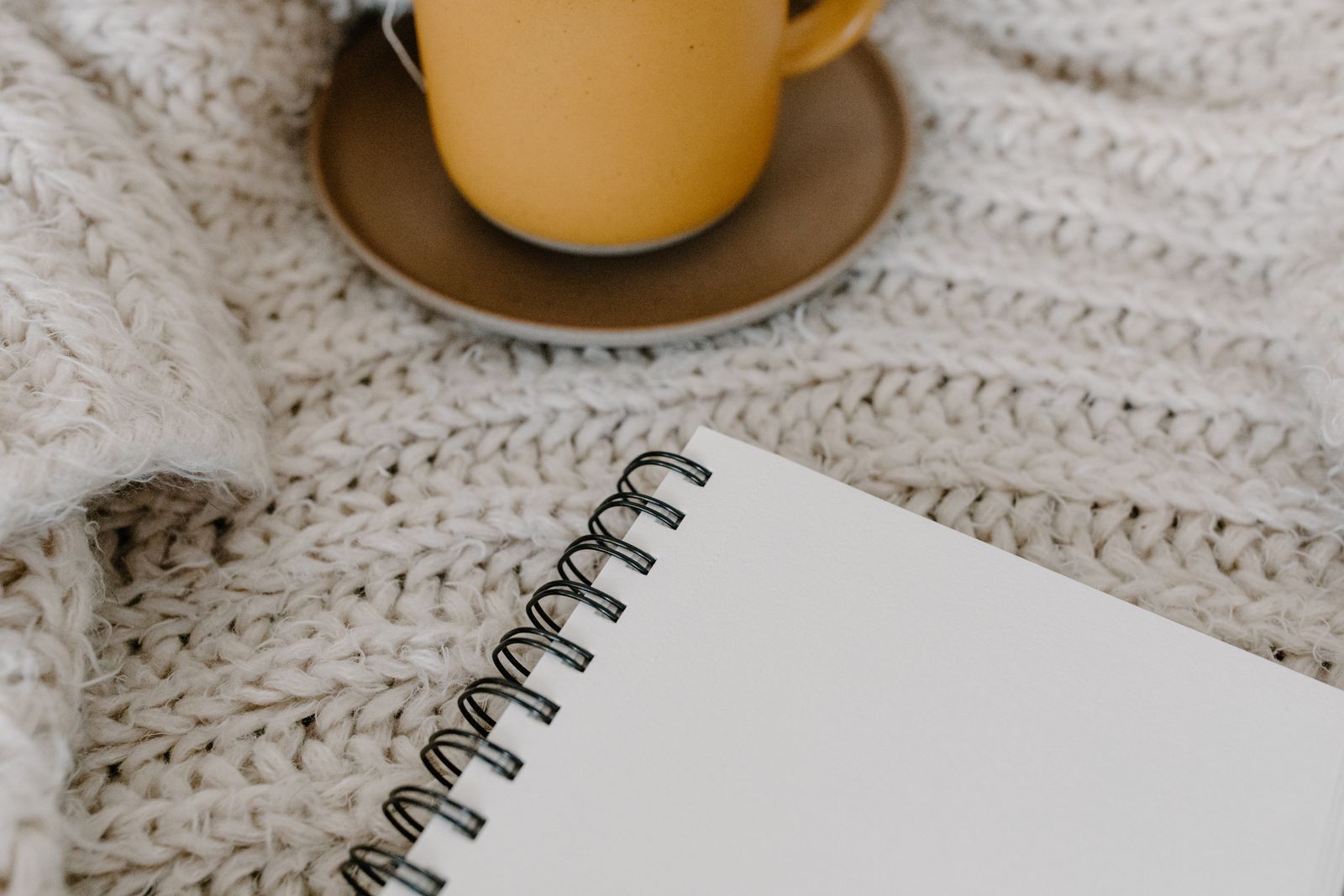 Warm cup of tea and notebook resting on a cozy knitted blanket, representing winter self-care after yoga practice