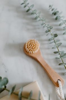 Wooden bath brush on a marble background with eucalyptus. Perfect for natural skincare routines.